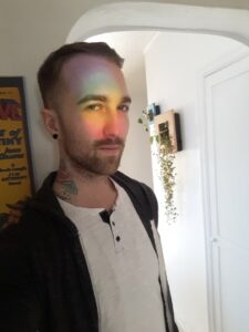 Psychic medium Chris Bennett with a rainbow prism across his face from a sun catcher
