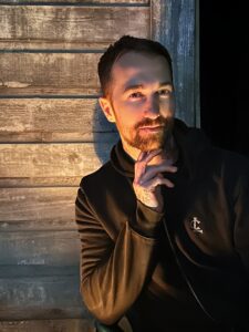 Chris Bennett in a black hoodie at night, candle glow on his face before a reading