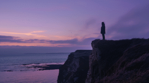 A silhouette on a cliff edge at twilight under lavender and gold sky, standing at the horizon of a new chapter