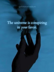 A silhouetted hand touching still water with the quote “The universe is conspiring in your favor.”